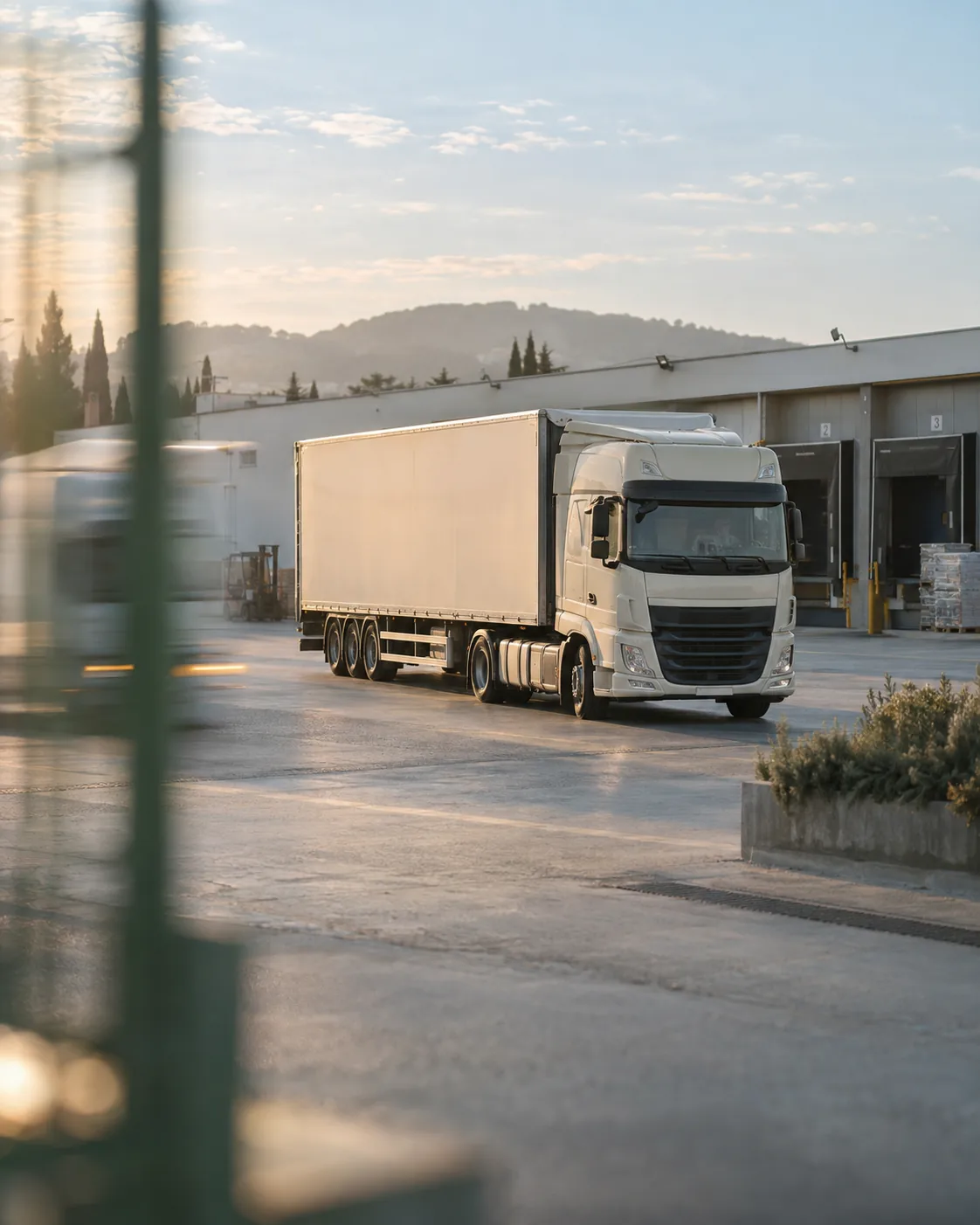 Ein heller Lastwagen fährt im weichen Morgenlicht in ein Logistikdepot